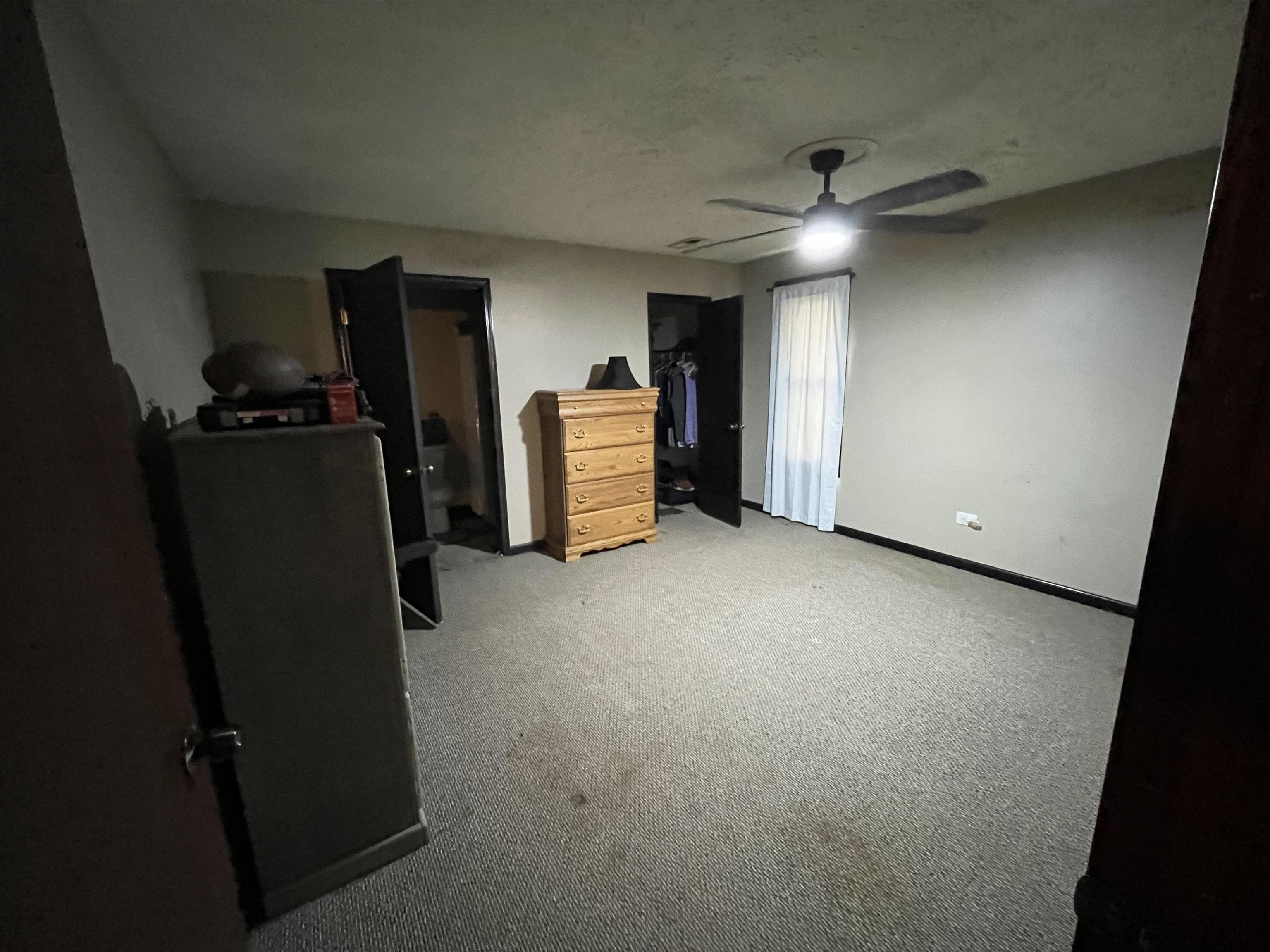 1125 Tyson Road Toone, TN 38381 - Photo 7 of 12 Carpeted room featuring a ceiling fan with integrated lighting, a window with vertical blinds, and a dark-framed open doorway revealing an interior space