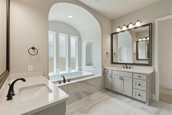 a bathroom with a tub sink double vanity granite and a tub