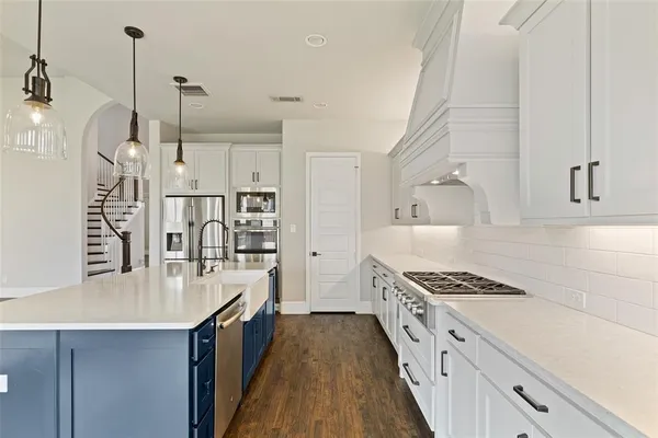 a kitchen with stainless steel appliances a stove a sink dishwasher a refrigerator and white cabinets with wooden floor