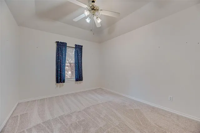 an empty room with chandelier fan and windows