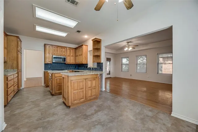 a view of kitchen with kitchen island granite countertop a stove a sink a refrigerator and white cabinets with wooden floor