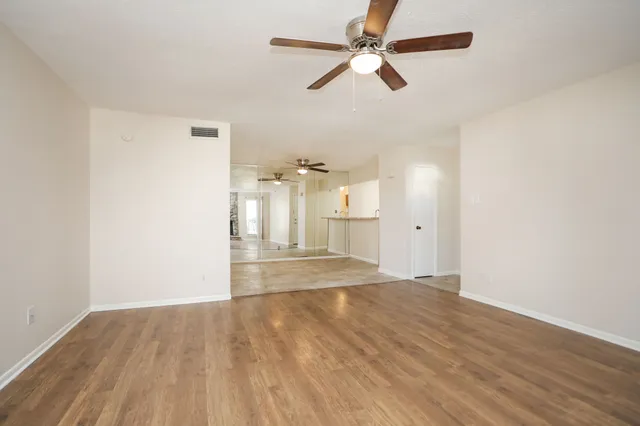 an empty room with wooden floor fan and windows