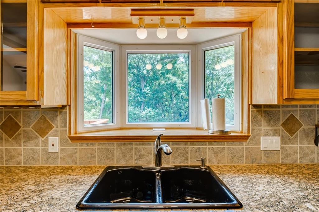 1600 Whitney Way Austin, TX 78741 - Photo 7 of 26 Kitchen featuring glass insert cabinets, decorative backsplash, light stone counters, and brown cabinets
