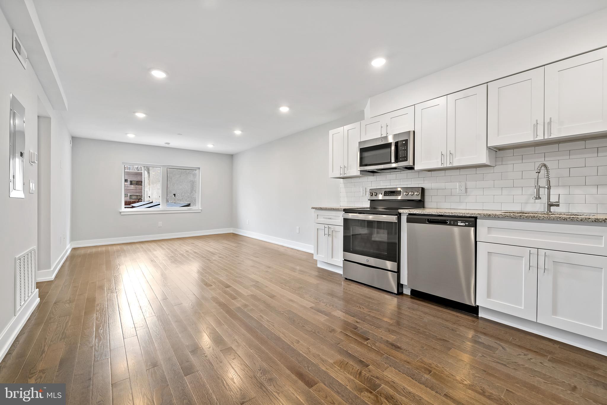1530 Palethorp Street, Unit 2B Philadelphia, PA 19122 - Photo 2 of 15 a kitchen with granite countertop a stove top oven a sink and white cabinets with wooden floor