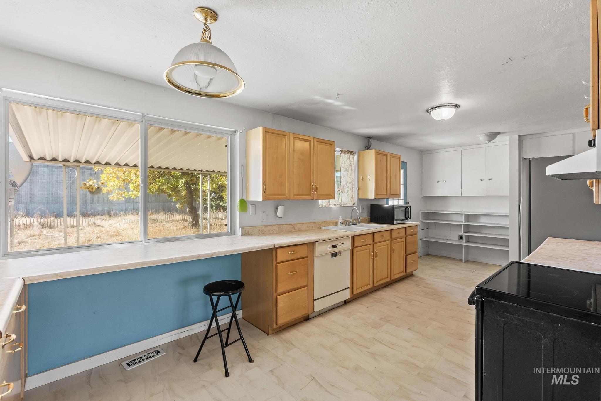 6295 West Grandview Place Boise, ID 83709 - Photo 11 of 29 Kitchen with black appliances, light countertops, decorative light fixtures, light brown cabinetry, and extractor fan