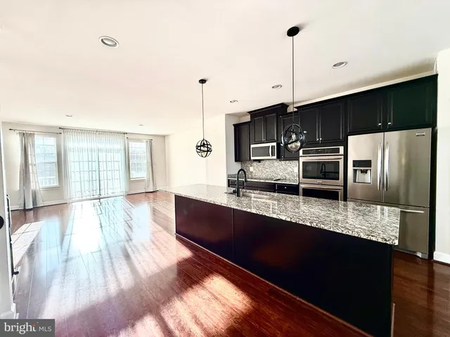 a kitchen with stainless steel appliances a sink a stove a refrigerator a center island with wooden floor