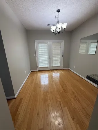 a view of an empty room with wooden floor and chandelier