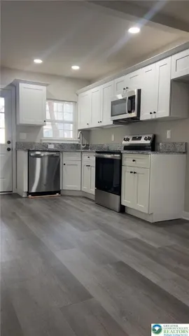 a large kitchen with granite countertop a stove top oven a sink dishwasher and a refrigerator with wooden floor