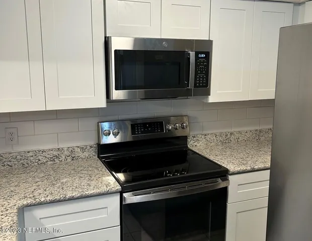 a kitchen with stainless steel appliances granite countertop white cabinets and a stove top oven