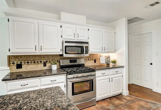 a kitchen with granite countertop white cabinets and stainless steel appliances
