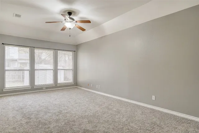 an empty room with chandelier fan and windows