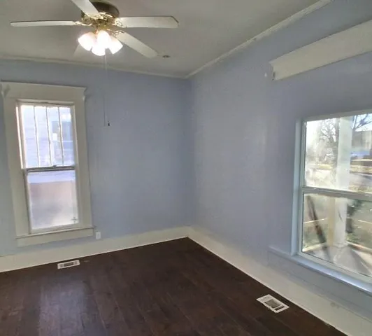 an empty room with wooden floor fan and windows