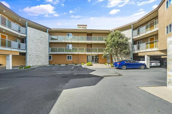 a front view of a building with a parking lot and large tree