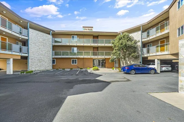 a front view of a building with a parking lot and large tree