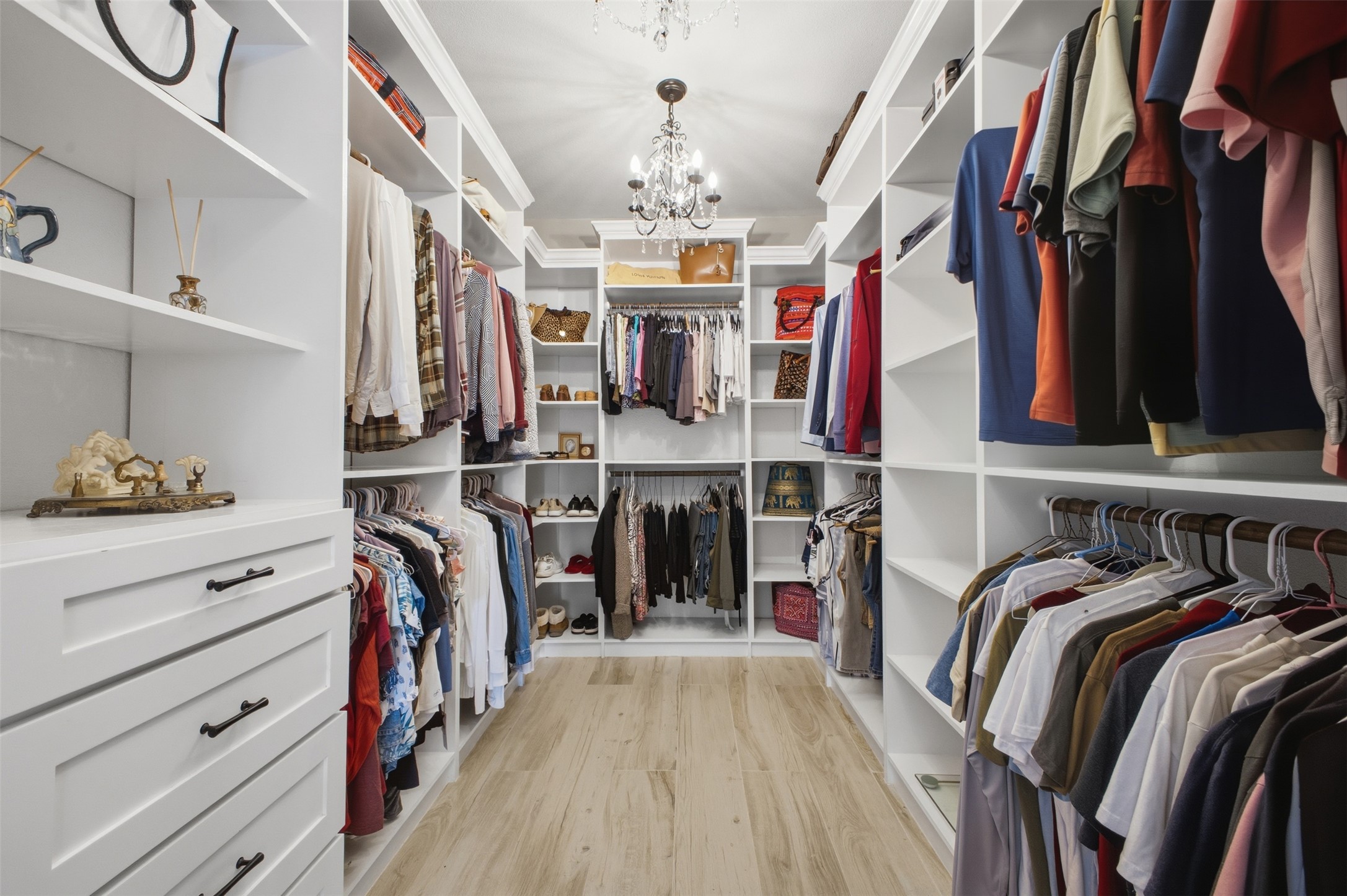 12710 Aries Loop Willis, TX 77318 - Photo 22 of 40 Expansive walk-in closet featuring extensive built-in shelving, hanging rods, and drawers, complemented by light wood flooring and an elegant chandelier