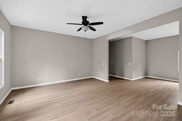 an empty room with wooden floor a ceiling fan and windows