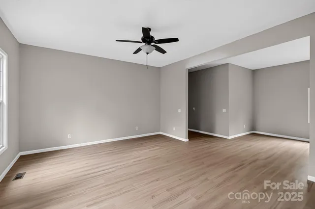 an empty room with wooden floor a ceiling fan and windows