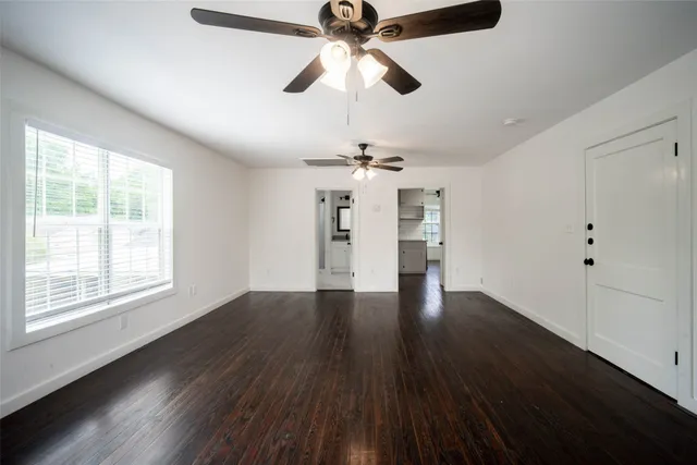 a view of an empty room with wooden floor ceiling fan and window