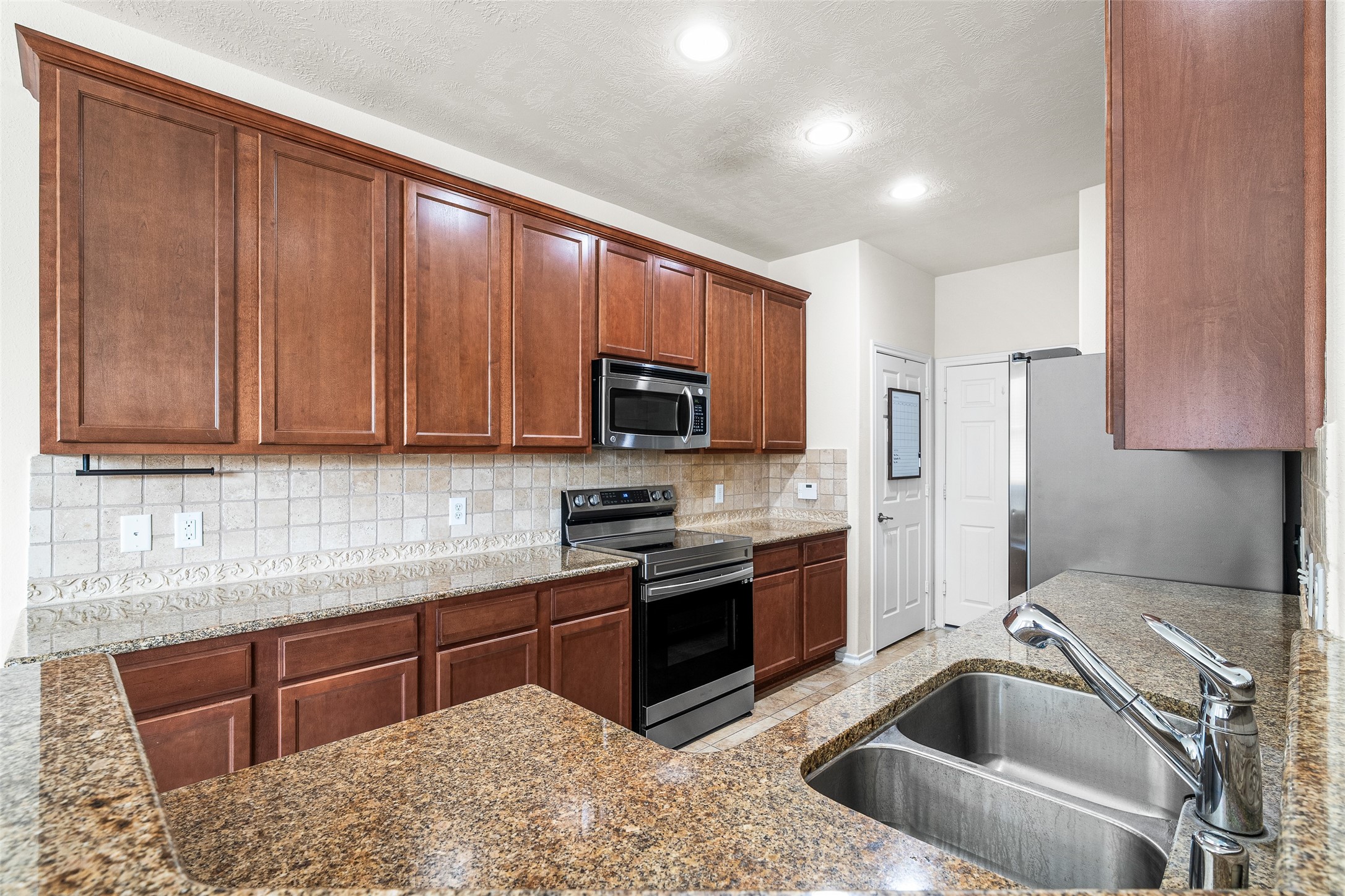 267 Bloomhill Place Magnolia, TX 77354 - Photo 4 of 19 This kitchen features classic natural wood-look cabinets, beautiful tile flooring, and a stylish peninsula that opens seamlessly to the living room — perfect for cooking, entertaining, and staying connected with guests.
