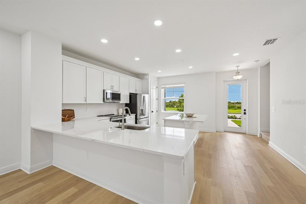 17712 Broadleaf Loop Venice, FL 34293 - Photo 3 of 23 a kitchen with stainless steel appliances a sink a stove a refrigerator cabinets and wooden floor