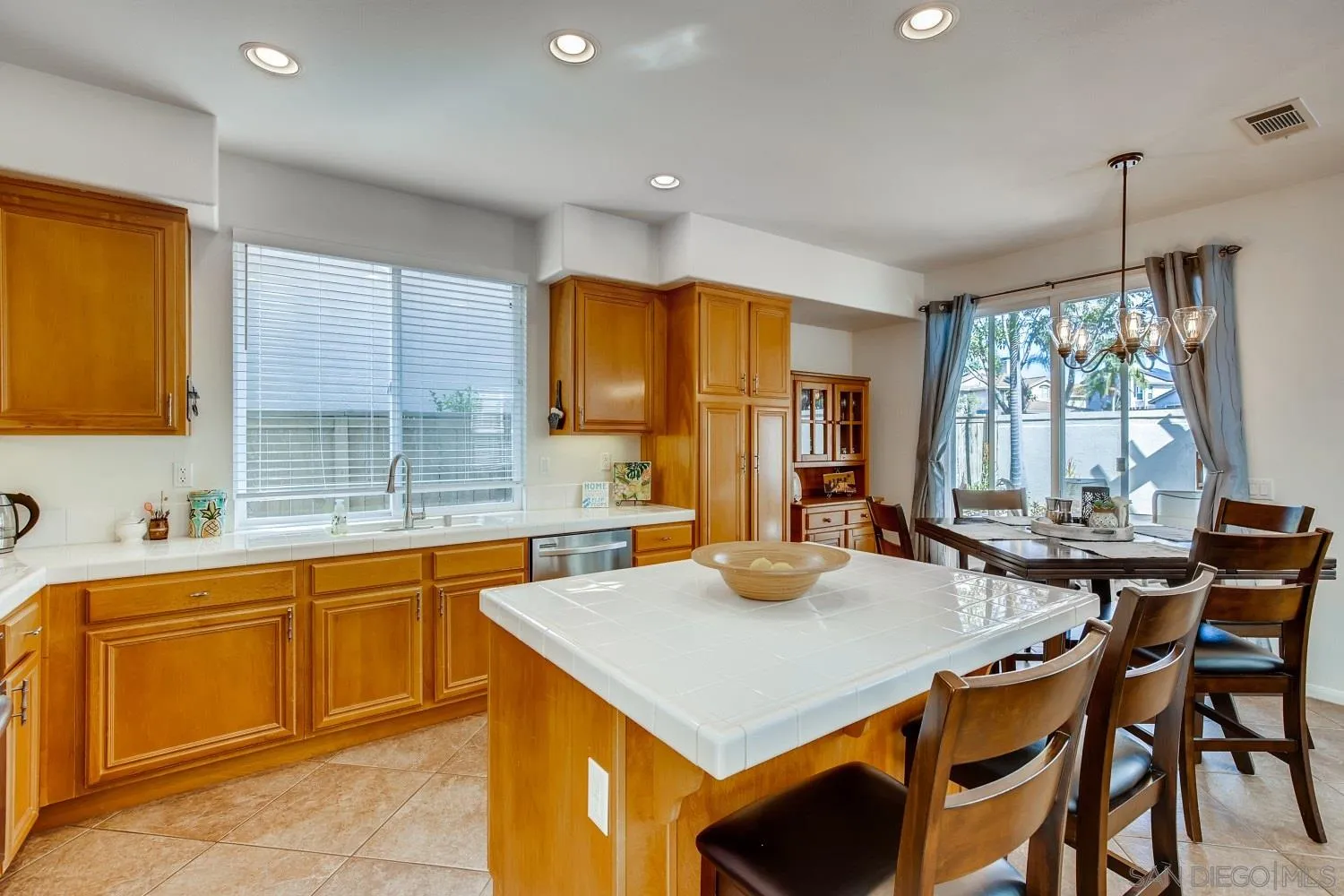 1332 Enchante Way Oceanside, CA 92056 - Photo 6 of 28 a kitchen with a stove a sink a kitchen island with chairs and wooden cabinets