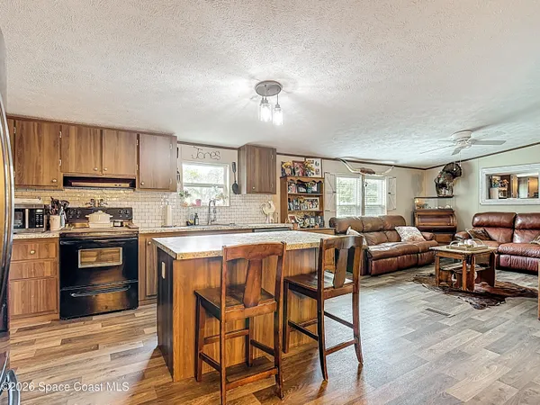 a kitchen with stainless steel appliances kitchen island granite countertop a stove a sink a refrigerator dining table and chairs with wooden floor