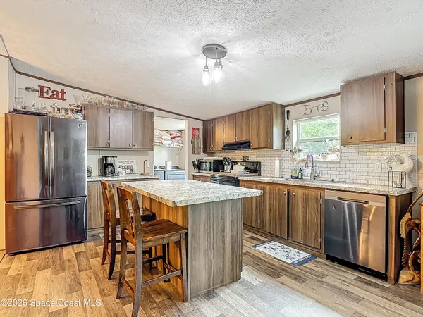 a kitchen with stainless steel appliances granite countertop a refrigerator a sink dishwasher a stove and white countertops with wooden floor