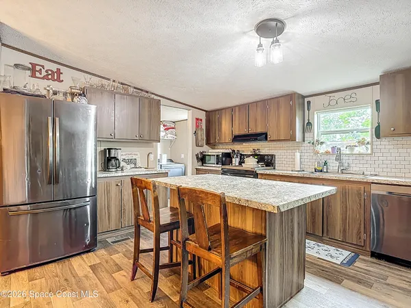 a kitchen with stainless steel appliances granite countertop a refrigerator a sink dishwasher a stove and white countertops with wooden floor
