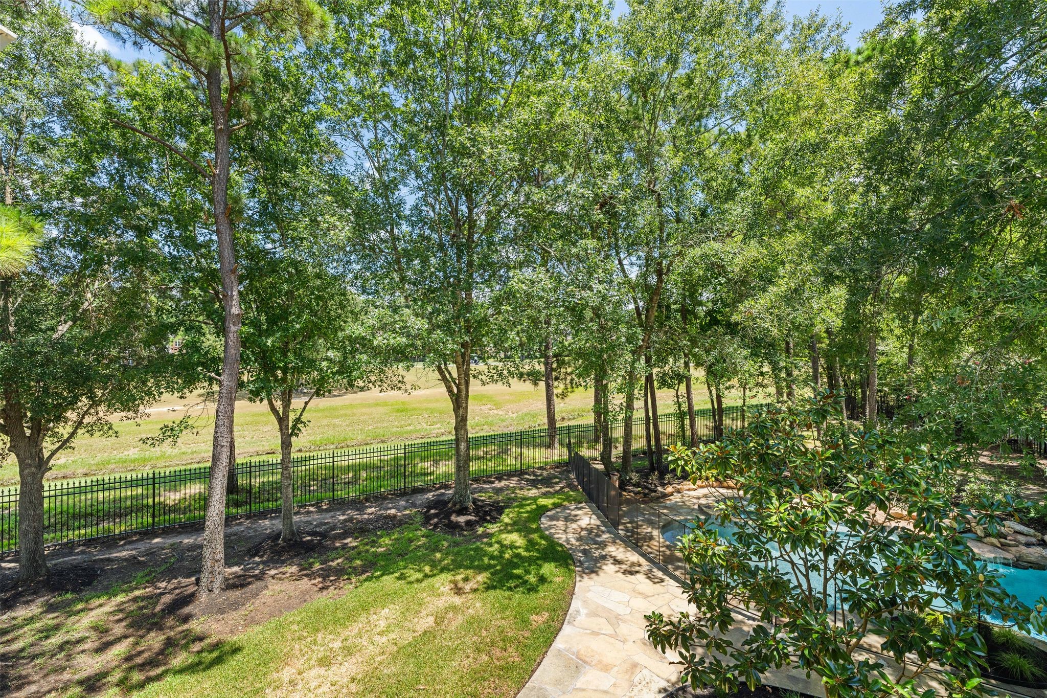 31 Hollymead Drive Spring, TX 77381 - Photo 3 of 50 This is the view from one of the two 2nd floor balconies overlooking the serene backyard with lush green landscape, mature trees providing shade, a clear view of the the golf course beyond a fence, and a glimpse of the pool surrounded by a stone patio. Perfect for nature lovers seeking privacy and relaxation.