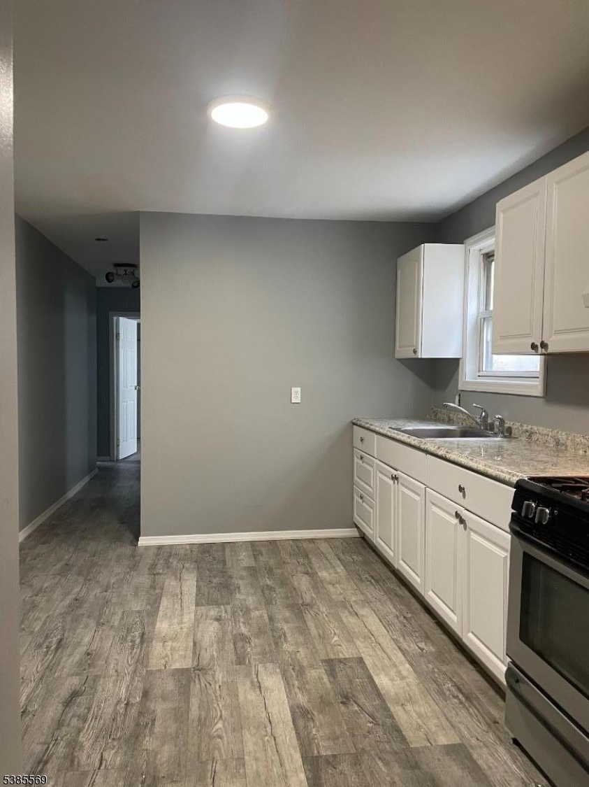 a kitchen with granite countertop a stove a sink and white cabinets