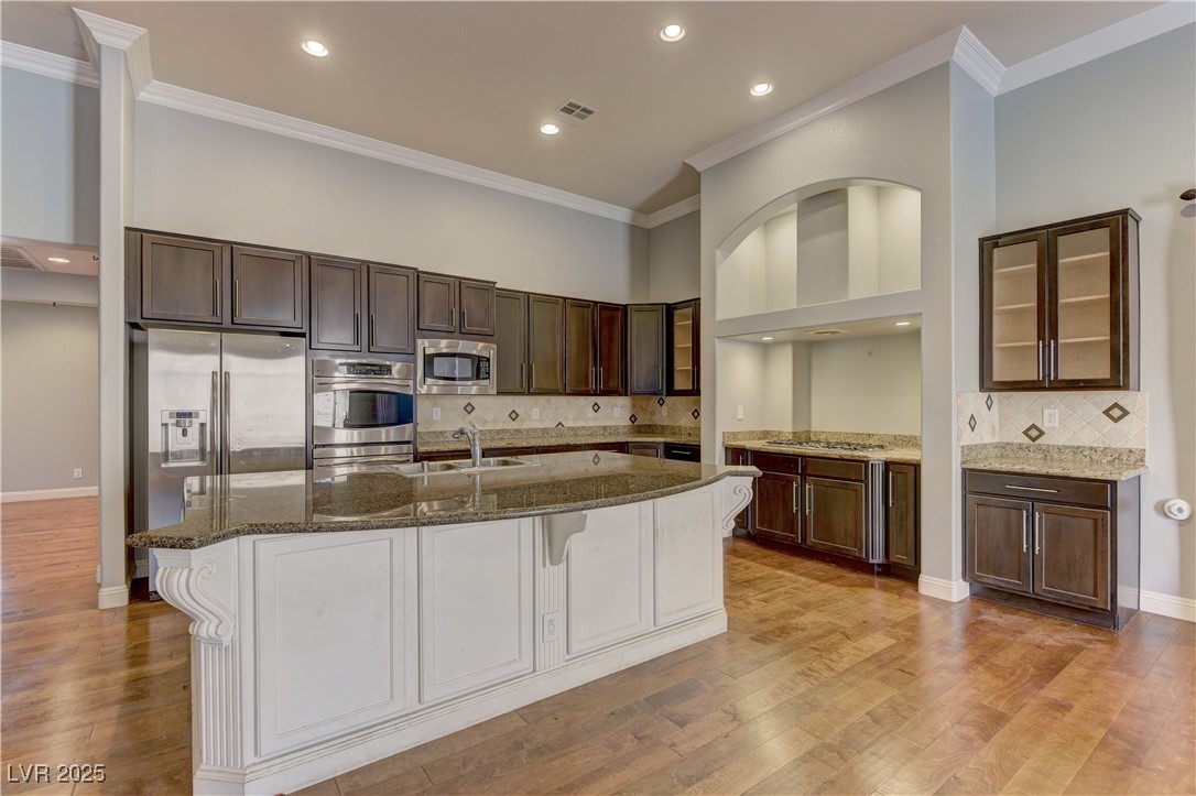 972 Rue Grand Paradis Lane Henderson, NV 89011 - Photo 7 of 32 Kitchen featuring dark wood finish cabinets, decorative backsplash, glass insert cabinets, dark stone countertops, and recessed lighting
