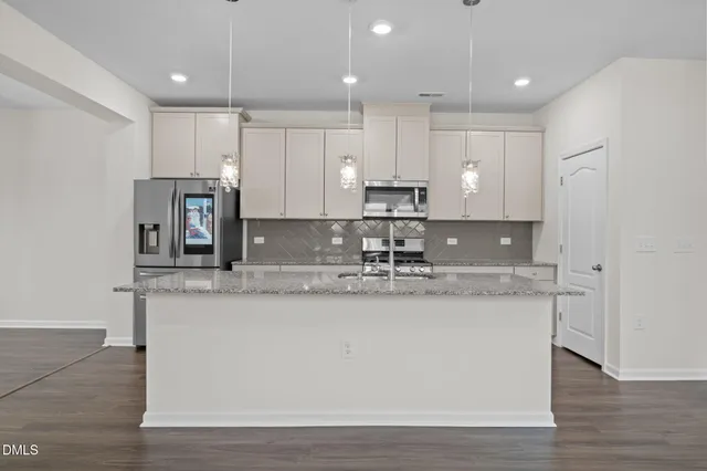 a large kitchen with stainless steel appliances granite countertop a sink a stove a refrigerator and white cabinets with wooden floor