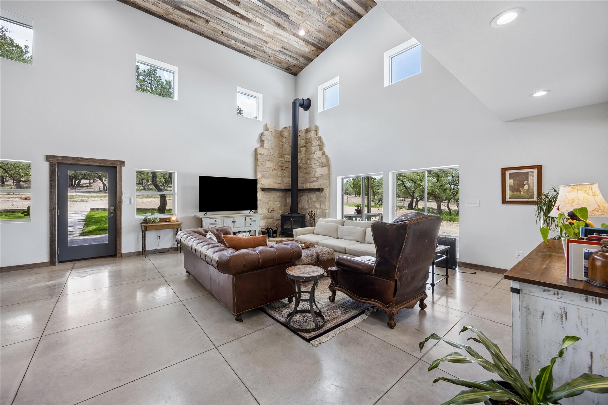 6411 West Fitzhugh Road Dripping Springs, TX 78620 - Photo 11 of 34 Great room featuring a vaulted wood-plank ceiling, polished concrete flooring, a stone fireplace with a stove, a full-light entry door with wood trim, and multiple high windows