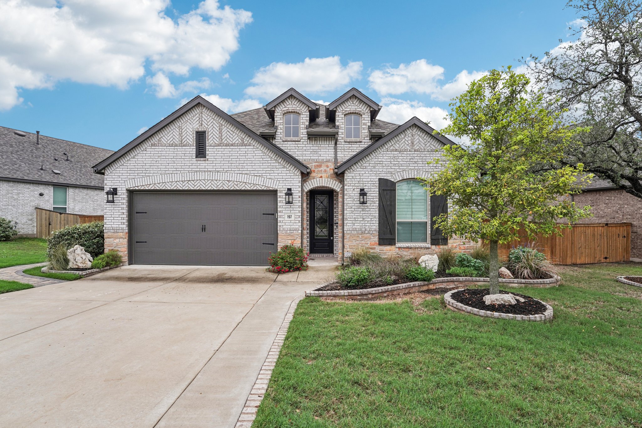 The property features a brick and stone exterior, an attached garage with a dark door, and a well-maintained lawn with landscaping