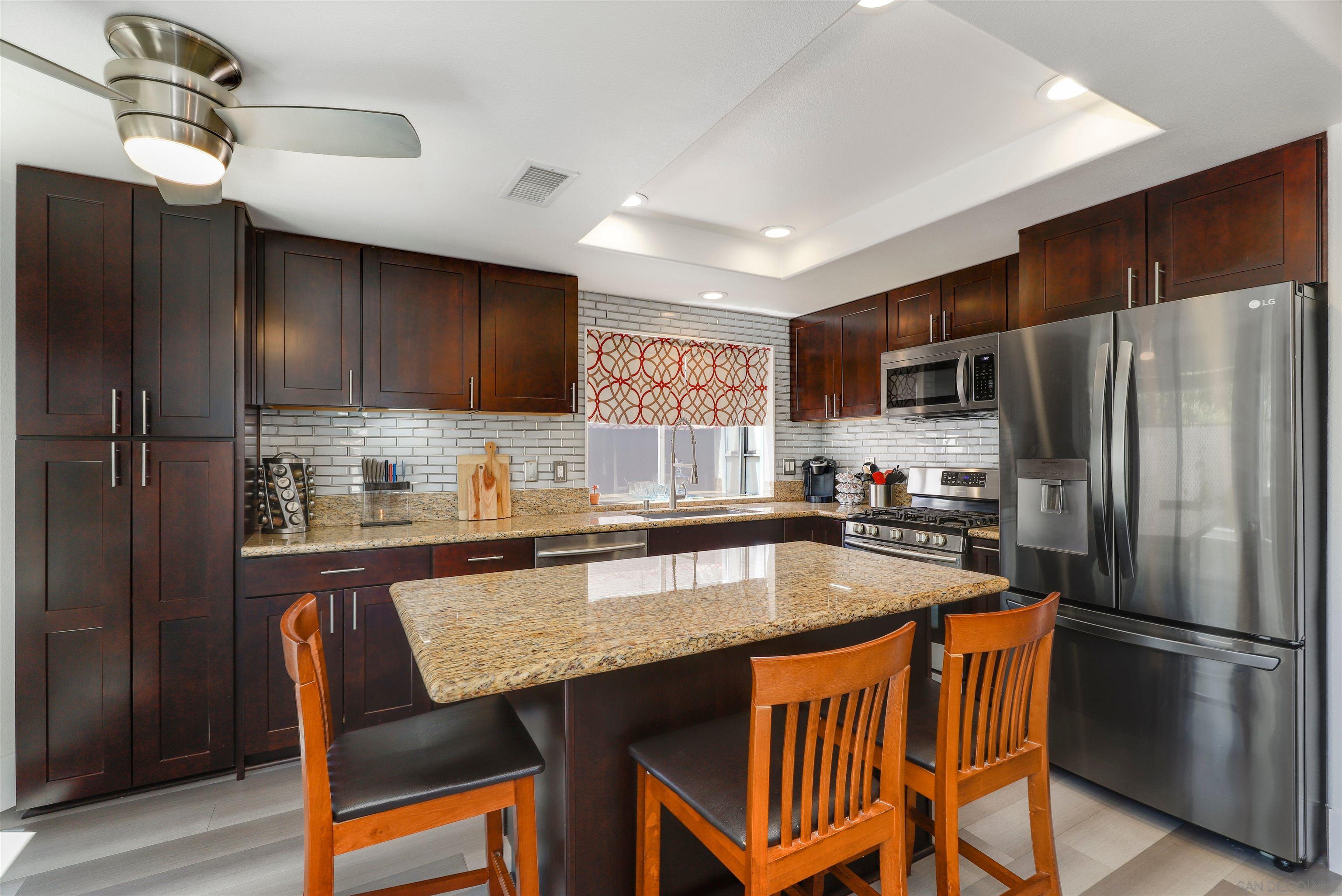 a kitchen with stainless steel appliances granite countertop a dining table chairs refrigerator and microwave
