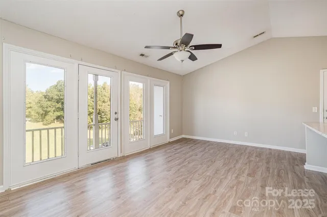 an empty room with wooden floor fan and windows