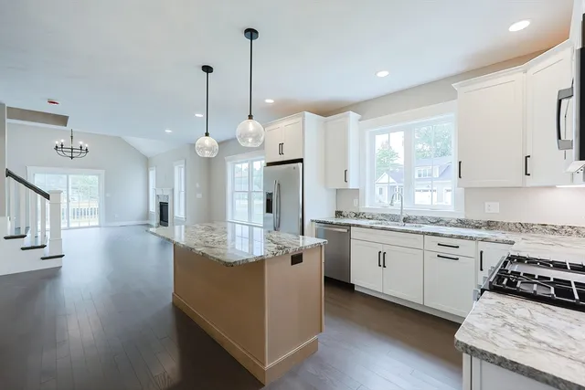 a kitchen with stainless steel appliances granite countertop a stove a sink dishwasher a refrigerator and white cabinets with wooden floor