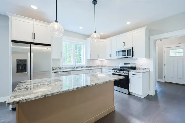 a large kitchen with granite countertop a stove a sink a center island a refrigerator and a wooden floor