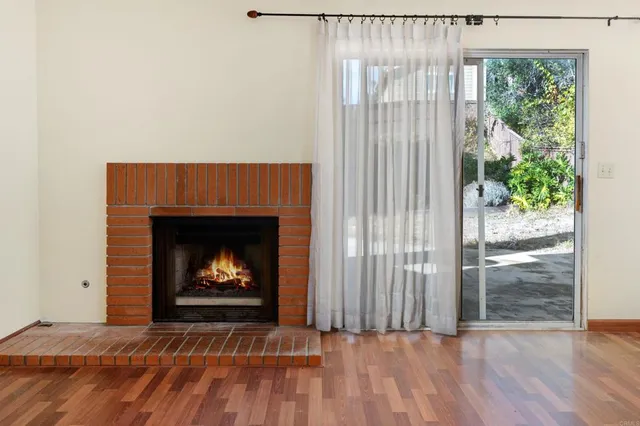 a view of an empty room with wooden floor fireplace and a window