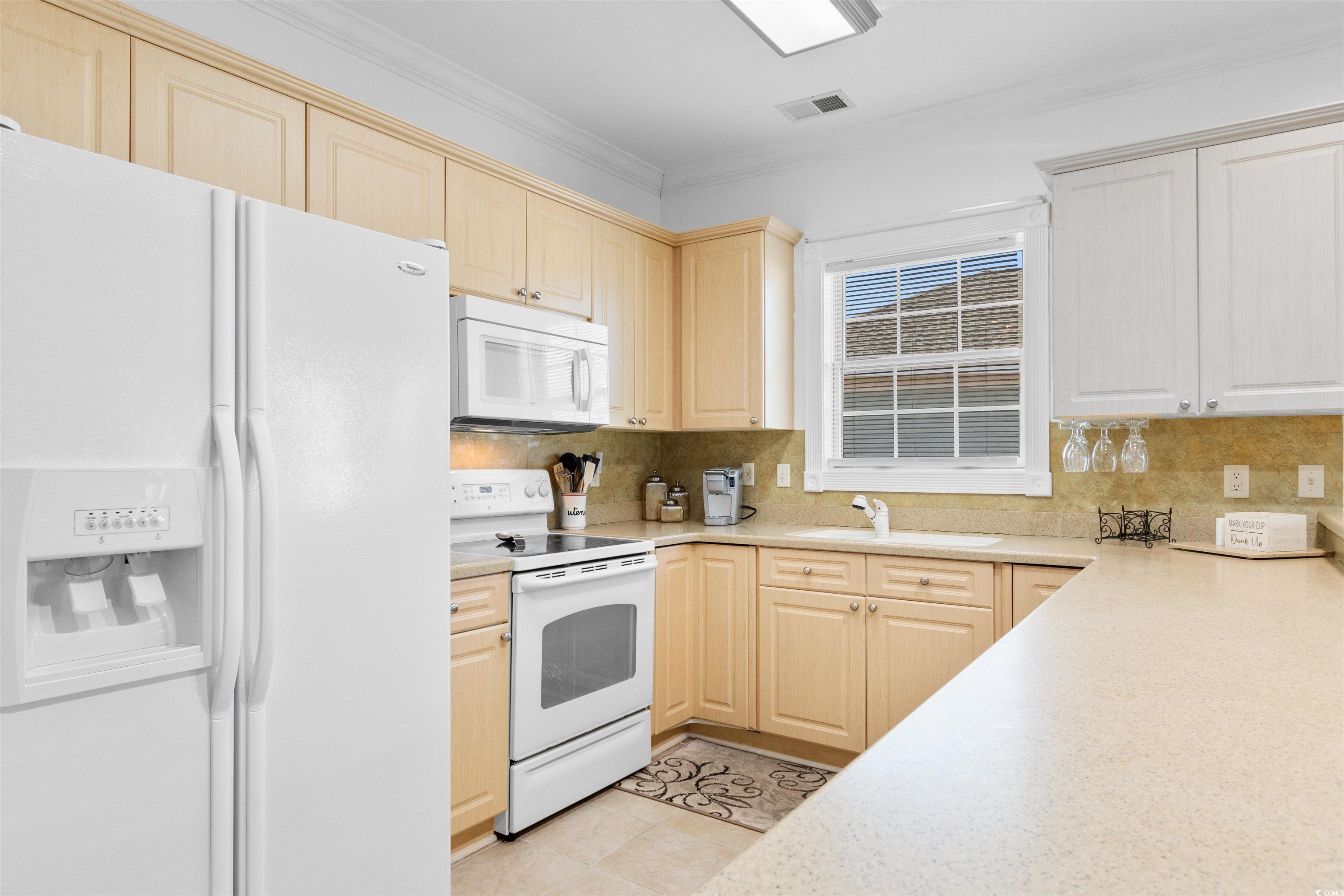 4891 Luster Leaf Circle, Unit 401 Myrtle Beach, SC 29577 - Photo 3 of 35 Kitchen with white appliances, crown molding, light brown cabinetry, decorative backsplash, and light tile patterned floors