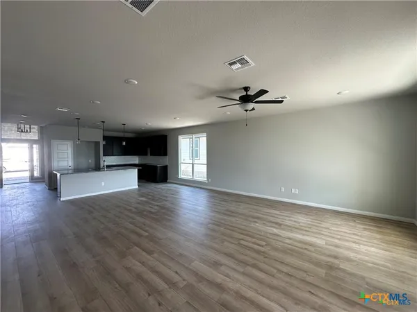 an empty room with wooden floor kitchen view and a window