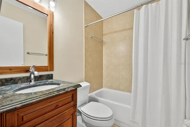 a bathroom with a granite countertop bathtub shower sink vanity mirror and toilet