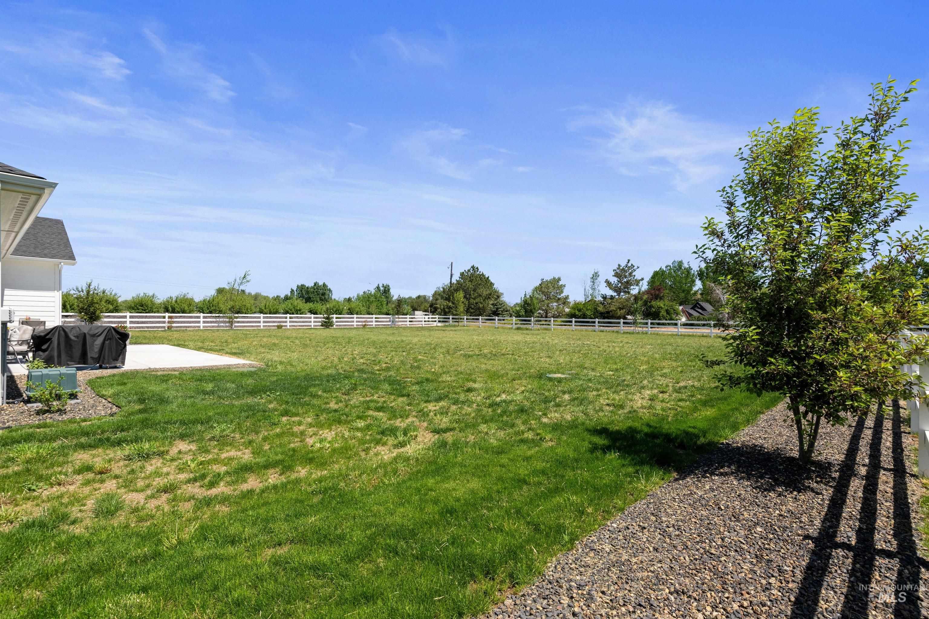 24990 Belgian Way Middleton, ID 83644 - Photo 40 of 50 Expansive rear lawn area featuring a white perimeter fence, a paved patio, and established trees