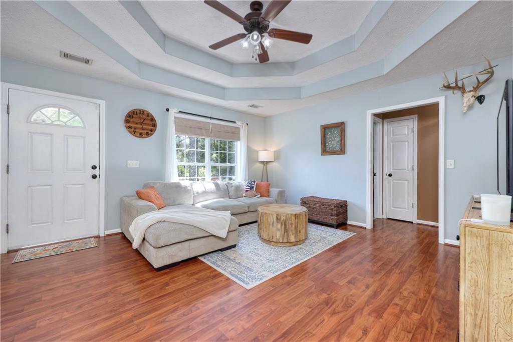 Living area featuring a raised ceiling, wood finished floors, a ceiling fan, and a textured ceiling