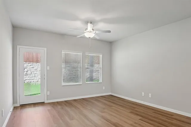 an empty room with wooden floor chandelier fan and windows