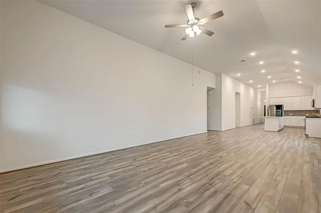 a view of an empty room with wooden floor and a ceiling fan