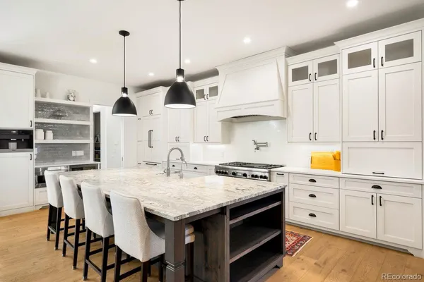 a kitchen with stainless steel appliances granite countertop a stove a sink refrigerator and white cabinets with wooden floor