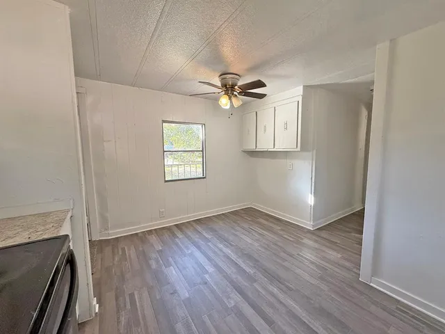 an empty room with wooden floor fan and windows