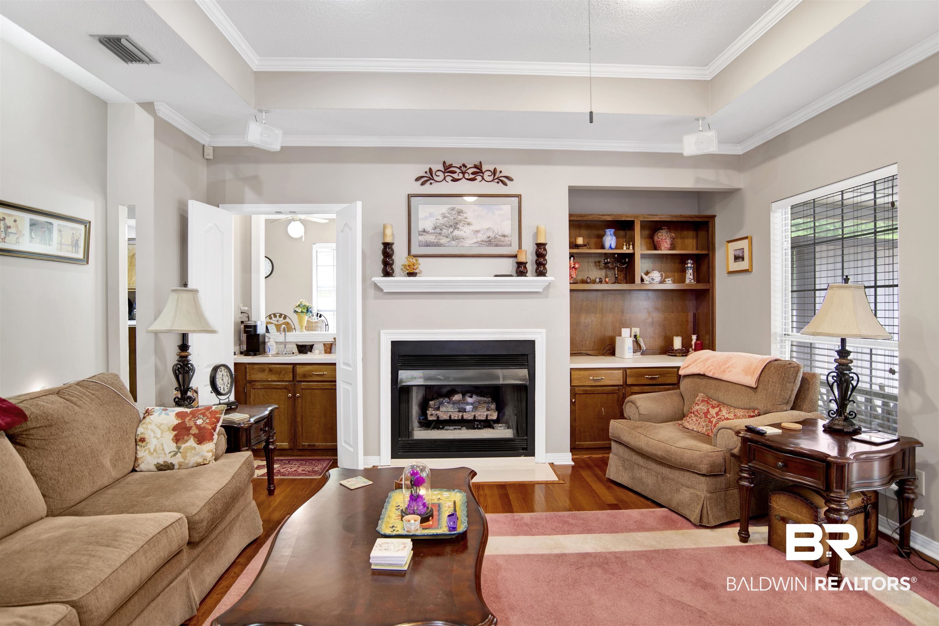 107 Virginia Circle Daphne, AL 36526 - Photo 11 of 47 Living area featuring a fireplace with a white mantel, built-in cabinetry, wood-finish flooring, a tray ceiling, and a large window with blinds
