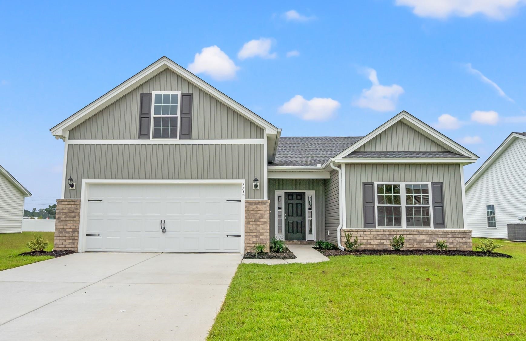 View of front of house featuring brick siding, board and batten siding, a front lawn, concrete driveway, and roof with shingles